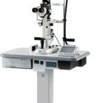 An Ophthalmic Slit Lamp Biomicroscope By Nidek Is Setup On A Height-Adjustable Table, Equipped With Binocular Eyepieces, Control Knobs, And An Attached Chin Rest For Patient Use. The Table Has A Control Panel And Sits On Wheels For Easy Mobility.