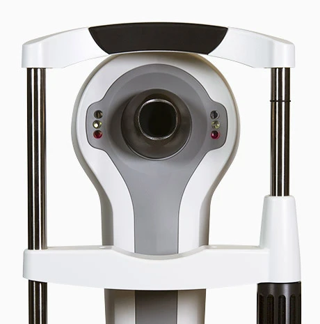 Close-Up Of A Nidek Ophthalmology Device With A Circular Opening In The Center, Surrounded By A White And Gray Frame. The Machine Features Two Vertical Black Rods On Either Side And Small Colored Indicators Beside The Opening. The Background Is Plain White.