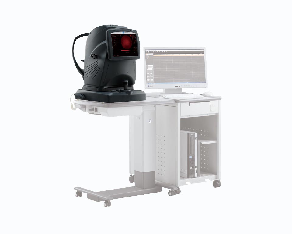 A Nidek Medical Imaging Device Consists Of A Black Scanner, A Computer Monitor Displaying A Red-Toned Image, And A Computer Unit Situated On A White Desk With Wheels. The Setup Is Likely Used For Eye Examinations Or Similar Diagnostic Purposes.