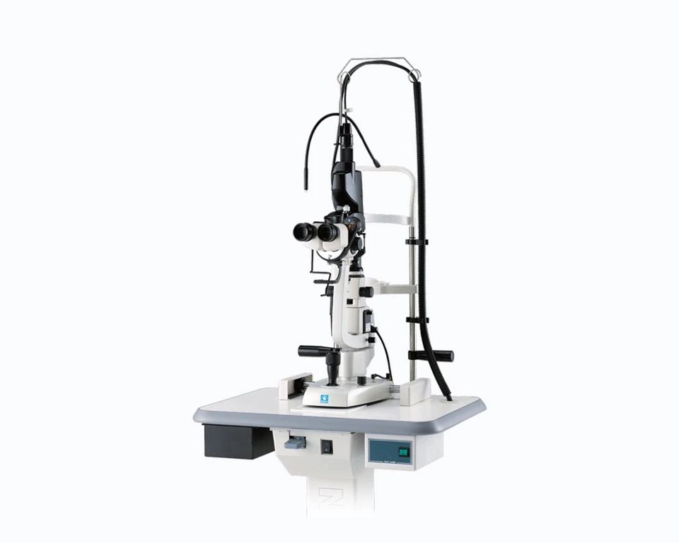 A Modern Nidek Ophthalmic Slit Lamp Used For Examining Eyes In A Clinical Setting. The Device Features Binocular Lenses For Stereoscopic Viewing, A Table Base With Control Panel, And An Attached Light Source For Illuminating The Eye During Examination.