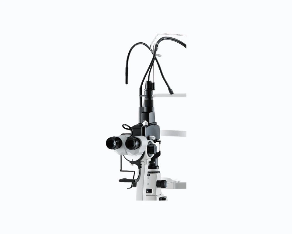 A Nidek Ophthalmic Slit Lamp, Used For Eye Examinations, Featuring Adjustable Binoculars And Various Controls, Mounted On A Stand. The Equipment Is White With Black Components And Has Cables Extending From The Top.