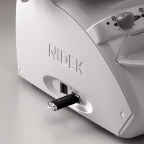 A White Nidek Medical Device With A Usb Flash Drive Inserted Into A Port On Its Side. The Smooth Surface Complements The Distinct Buttons And Control Elements Visible On The Upper Part, Exemplifying Nidek’s Commitment To Seamless Design And Functionality.