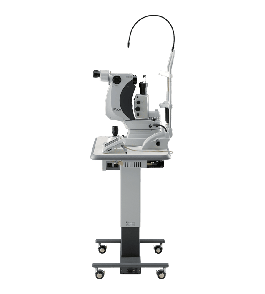 A White And Gray Nidek Ophthalmic Slit Lamp Microscope, Used For Detailed Examination Of The Eye, Is Mounted On A Height-Adjustable Rolling Stand. The Device Features Binocular Eyepieces, A Joystick, And A Chin Rest For The Patient.