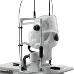 A High-Tech Eye Examination Machine By Nidek, Featuring Multiple Adjustable Components, A Headrest, And Various Lenses. The Equipment Is Designed For Detailed Eye Health Assessments And Is Placed On A Medical Imaging Unit. Wires Extend From The Top For Connectivity.