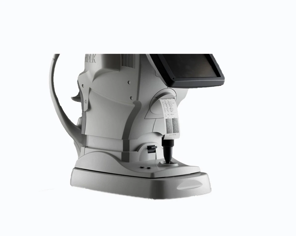 A Gray, High-Tech Nidek Optometry Instrument With A Digital Display And Control Panel Used For Eye Examinations Is Pictured. The Design Includes Various Knobs, A Chin Rest, And A Lens Area For Conducting Eye Tests. The Background Is Plain White.