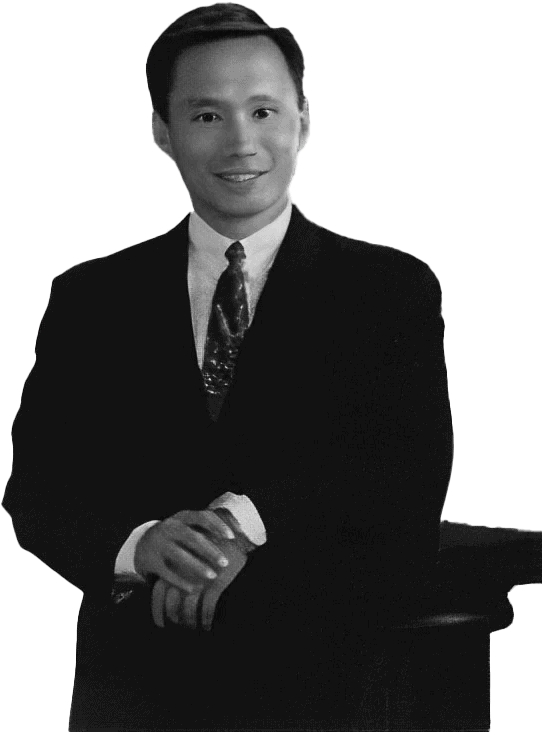 Black-And-White Photograph Of A Person Wearing A Suit And Tie, Standing With Hands Clasped And Resting On A Nidek Podium. The Person Has A Slight Smile And Short, Neatly Styled Hair. The Background Is Plain.